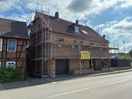 Gebäude mit Baugerüst und Fassadenarbeiten, neben einem traditionellen Fachwerkhaus.