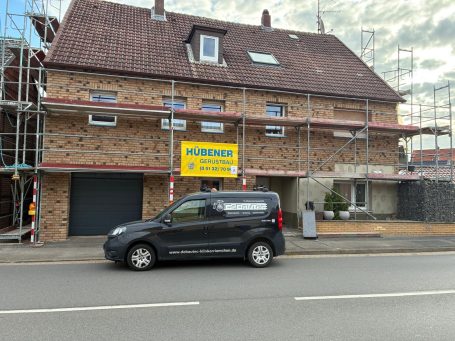 Gestecktes Gebäude mit Baugerüst, beschildert für Renovierungsarbeiten. Firmenfahrzeug parkt davor.