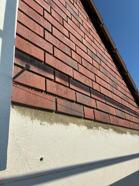 Dachfläche mit roten Klinkerriemchen und einem hellen Putz unter blauem Himmel.