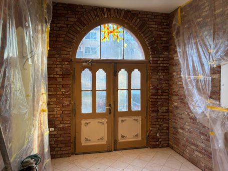 Eingangsbereich mit Doppeltür aus Holz, Klinkerriemchen Wänden und einem Lichtfenster darüber.