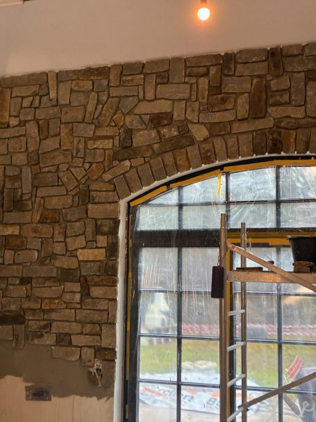 Steinmauer mit Bogen und großen Fenstern, Aufbau eines Gerüsts im Vordergrund.