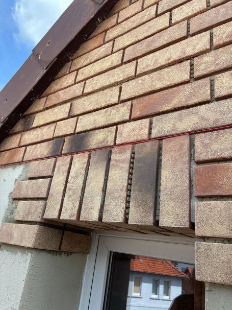 Klinkerriemchen an einem Dachüberstand und Fensterrahmen mit blauen Himmel im Hintergrund.