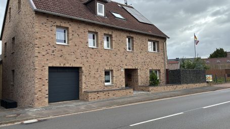 Zweistöckiges, geklinkertes Haus mit Garagentür und Fahne vor dem Eingang.